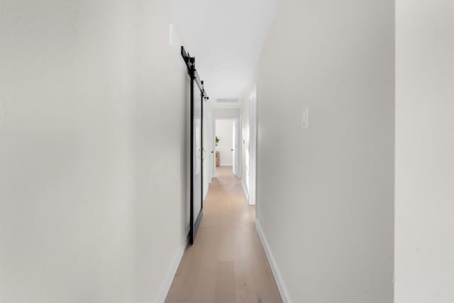 corridor with a barn door and light hardwood / wood-style flooring