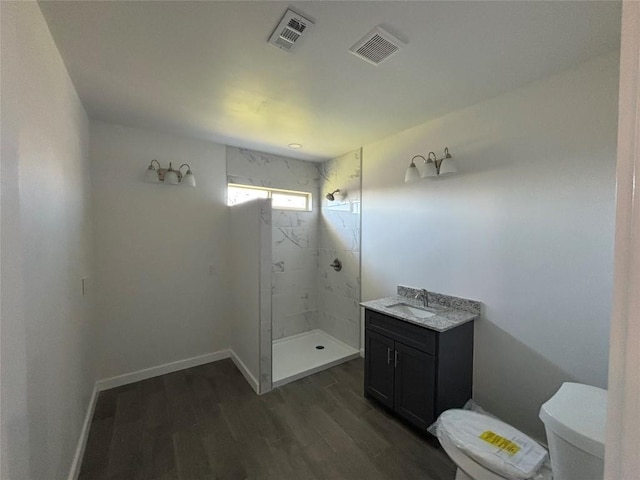 bathroom with wood-type flooring, toilet, vanity, and a tile shower