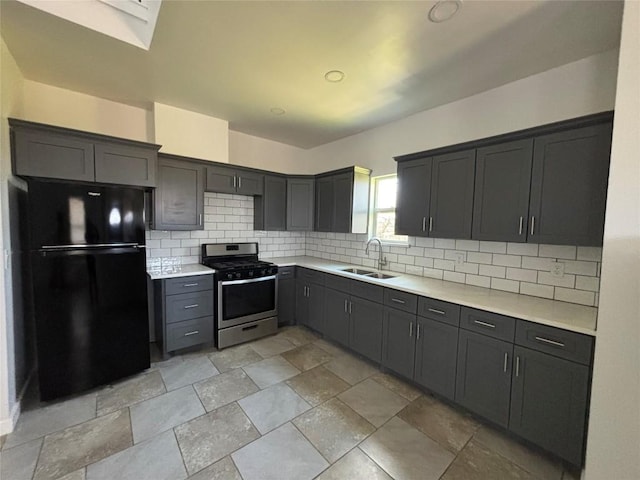 kitchen featuring black refrigerator, sink, decorative backsplash, and stainless steel gas range oven