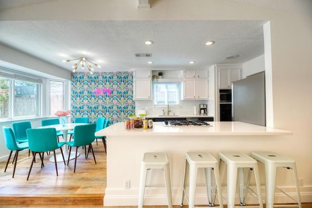 kitchen featuring appliances with stainless steel finishes, white cabinets, a kitchen bar, light hardwood / wood-style floors, and kitchen peninsula