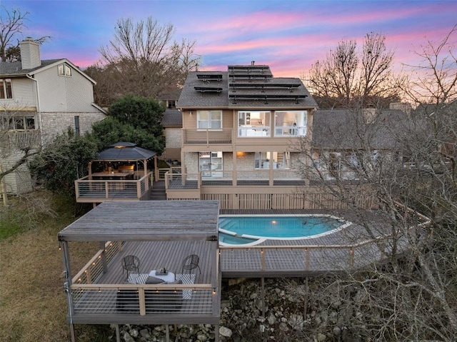 back house at dusk with a gazebo, a balcony, and a swimming pool side deck