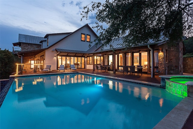 pool at dusk with a patio and an in ground hot tub