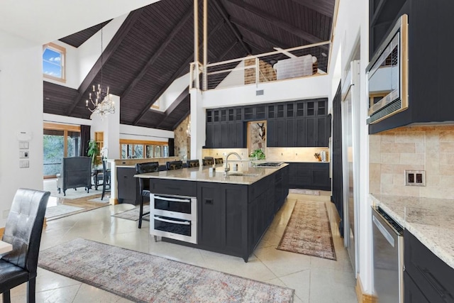 kitchen featuring high vaulted ceiling, sink, backsplash, a center island with sink, and beam ceiling