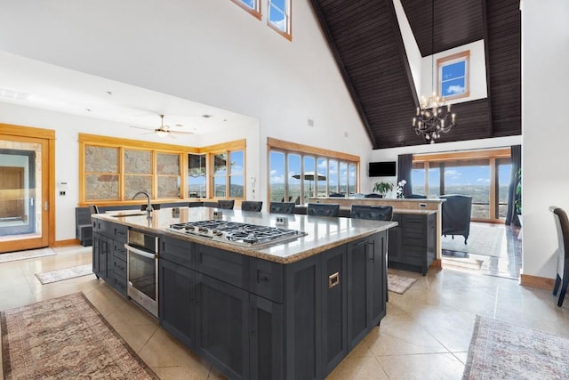 kitchen with sink, light stone counters, appliances with stainless steel finishes, a kitchen island, and a towering ceiling