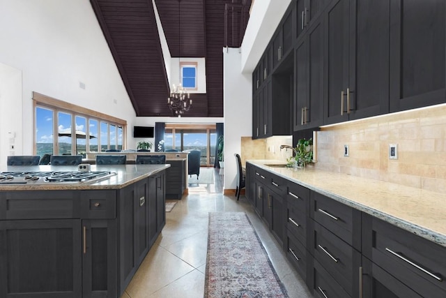 kitchen with light stone counters, a notable chandelier, stainless steel gas cooktop, light tile patterned flooring, and decorative backsplash