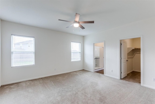 unfurnished bedroom with ensuite bathroom, a walk in closet, light colored carpet, and ceiling fan