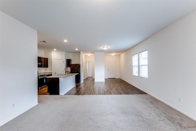 kitchen with an island with sink, sink, dark carpet, and black appliances