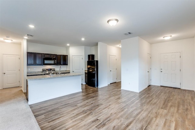 kitchen with sink, a kitchen island with sink, dark brown cabinetry, black appliances, and light wood-type flooring