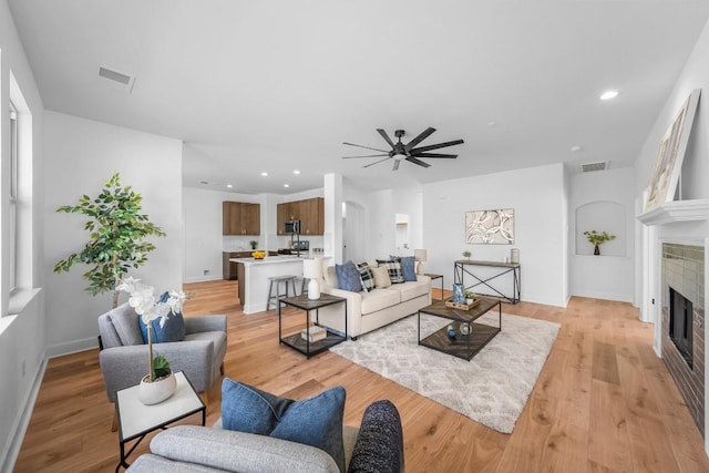 living room featuring a fireplace, light hardwood / wood-style floors, and ceiling fan