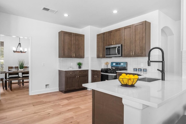 kitchen featuring sink, light hardwood / wood-style flooring, black range with gas stovetop, kitchen peninsula, and pendant lighting