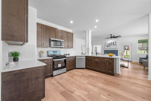 kitchen with sink, decorative backsplash, light hardwood / wood-style floors, kitchen peninsula, and stainless steel appliances