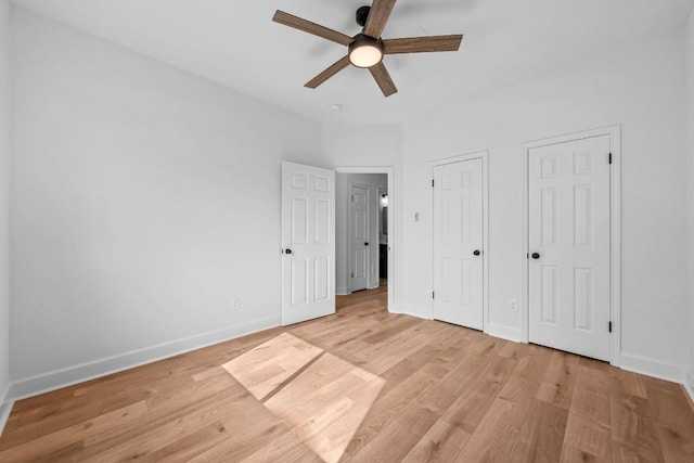 unfurnished bedroom with ceiling fan, two closets, and light wood-type flooring