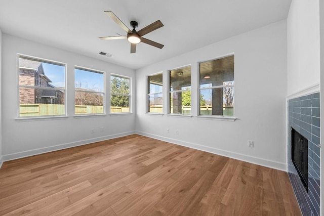 unfurnished living room with a tiled fireplace, ceiling fan, and light wood-type flooring