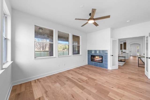 unfurnished living room with a tiled fireplace, ceiling fan, and light wood-type flooring