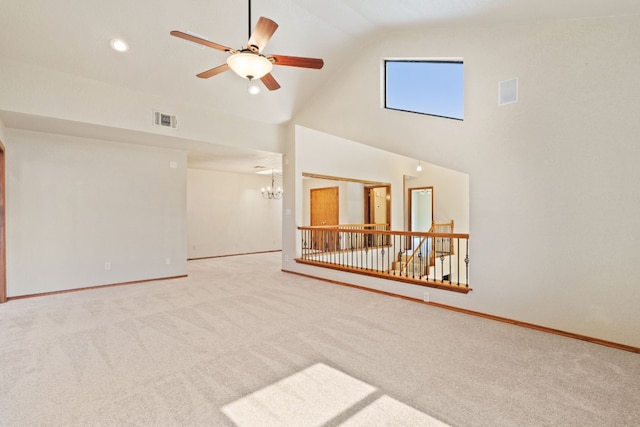 unfurnished living room with ceiling fan with notable chandelier, high vaulted ceiling, and carpet