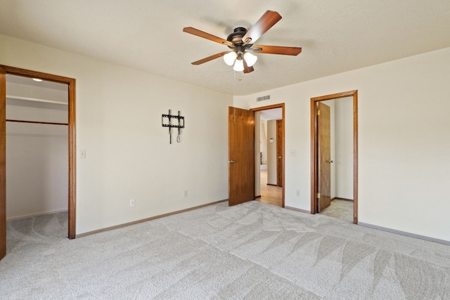 unfurnished bedroom with ceiling fan, light colored carpet, a spacious closet, and a closet