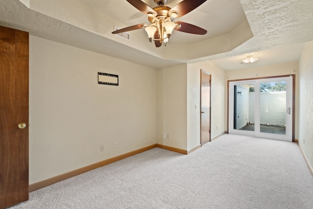 carpeted empty room with ceiling fan, a tray ceiling, and a textured ceiling