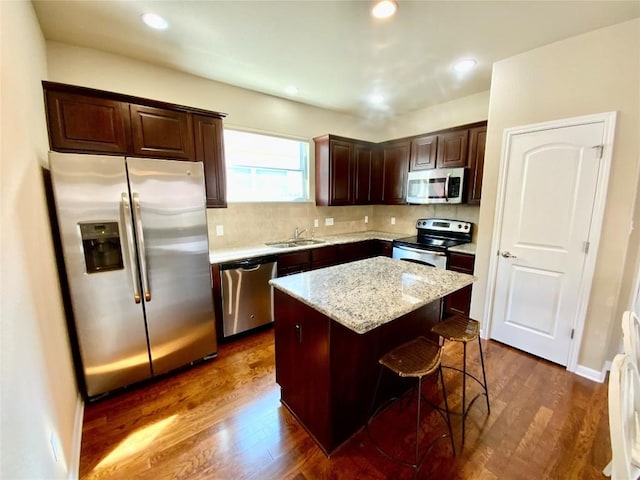 kitchen featuring sink, appliances with stainless steel finishes, dark hardwood / wood-style floors, a kitchen island, and light stone countertops