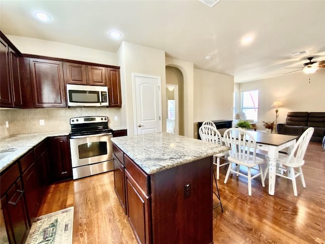 kitchen featuring a kitchen island, light stone countertops, appliances with stainless steel finishes, and hardwood / wood-style flooring