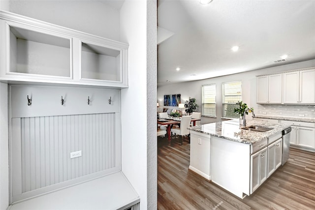 kitchen with hardwood / wood-style floors, white cabinetry, sink, a kitchen island with sink, and light stone countertops