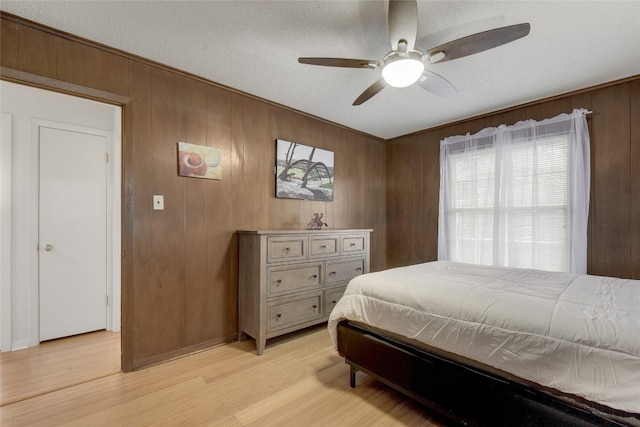 bedroom featuring ornamental molding, wooden walls, light hardwood / wood-style floors, and a textured ceiling