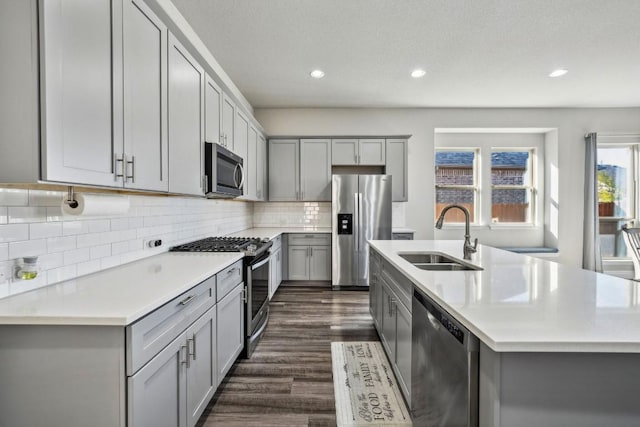 kitchen with sink, appliances with stainless steel finishes, gray cabinetry, dark hardwood / wood-style floors, and a center island with sink