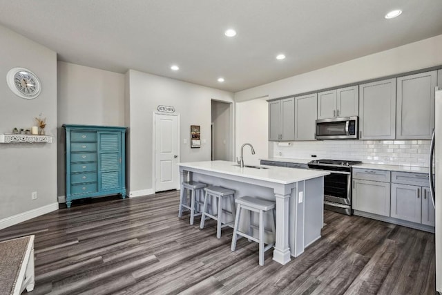 kitchen featuring gray cabinets, appliances with stainless steel finishes, a breakfast bar, sink, and a kitchen island with sink