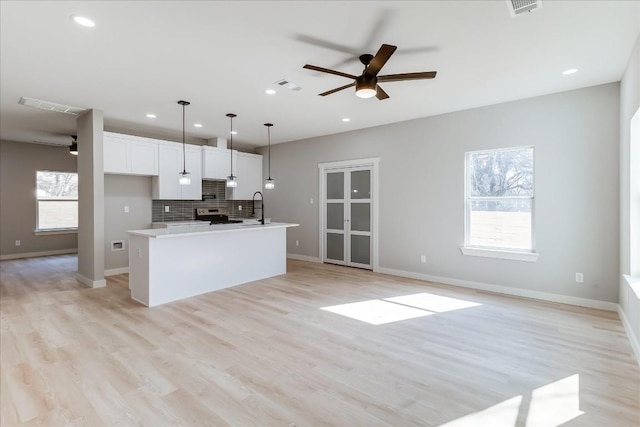 kitchen featuring hanging light fixtures, electric range, white cabinets, a kitchen island with sink, and backsplash