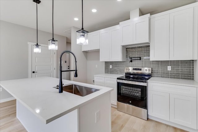 kitchen with sink, stainless steel range with electric stovetop, decorative light fixtures, an island with sink, and white cabinets