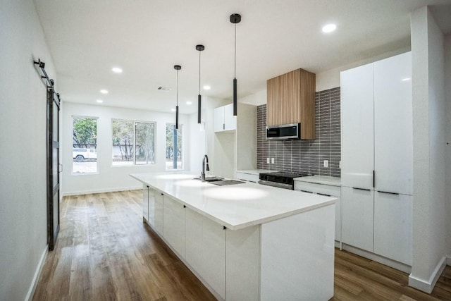 kitchen featuring white cabinetry, hanging light fixtures, appliances with stainless steel finishes, an island with sink, and a barn door