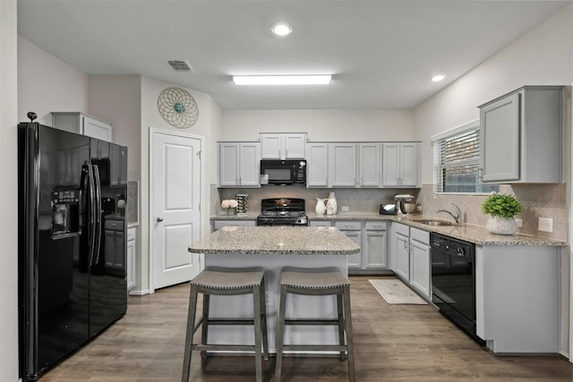 kitchen with tasteful backsplash, visible vents, a sink, wood finished floors, and black appliances