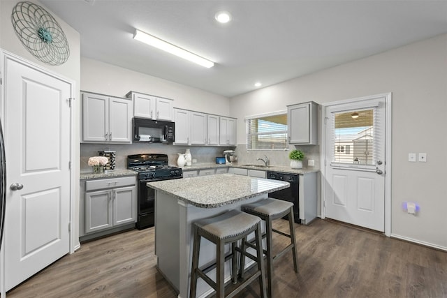 kitchen featuring a kitchen breakfast bar, black appliances, decorative backsplash, and gray cabinetry