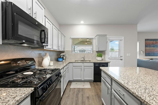 kitchen featuring black appliances, light stone counters, backsplash, and wood finished floors