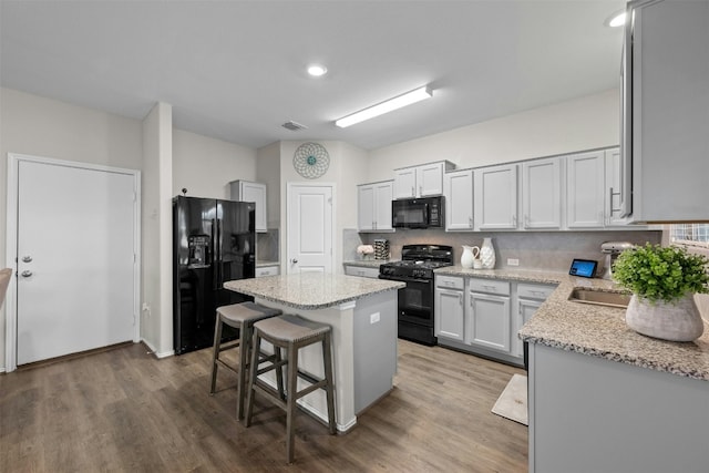 kitchen with decorative backsplash, a center island, black appliances, and light stone countertops