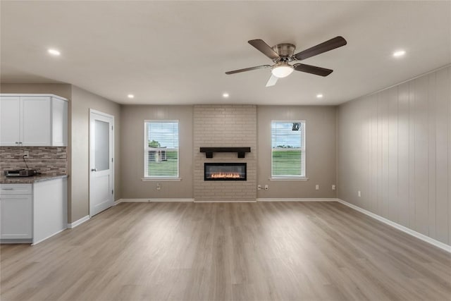 unfurnished living room with ceiling fan, a healthy amount of sunlight, a fireplace, and light wood-type flooring