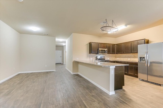 kitchen featuring dark brown cabinetry, kitchen peninsula, stainless steel appliances, light hardwood / wood-style floors, and backsplash