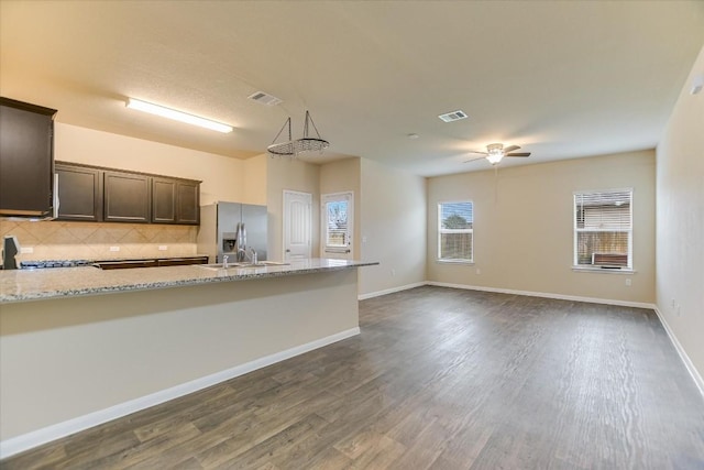 kitchen featuring dark wood-type flooring, dark brown cabinets, light stone counters, tasteful backsplash, and stainless steel fridge with ice dispenser