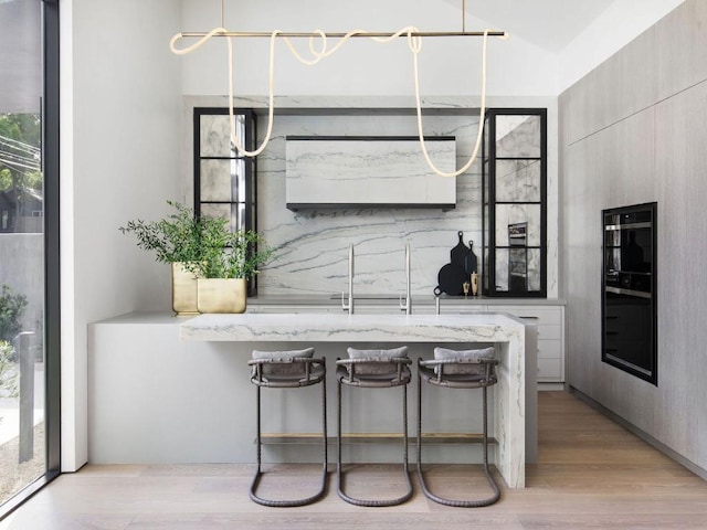 kitchen featuring hanging light fixtures, light wood-type flooring, light stone countertops, and a kitchen bar