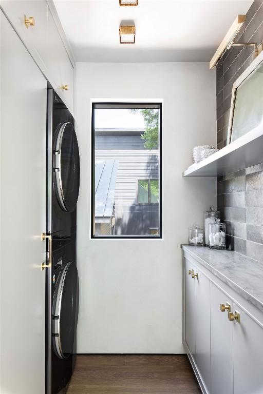 laundry area featuring cabinets, stacked washer / drying machine, and dark hardwood / wood-style floors