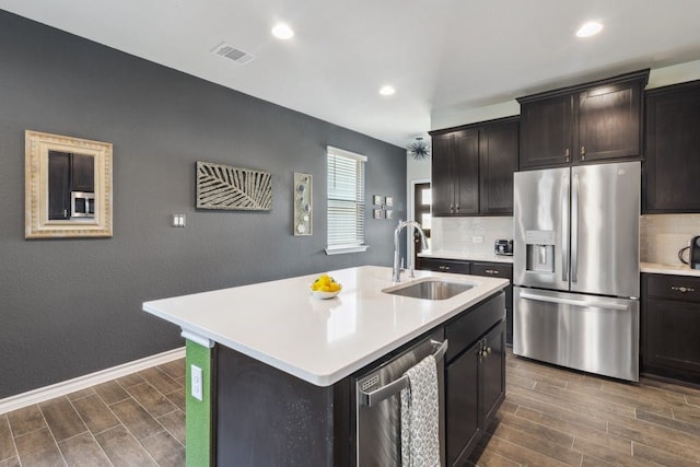 kitchen featuring appliances with stainless steel finishes, a kitchen island with sink, sink, and decorative backsplash