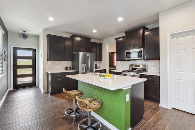 kitchen featuring a breakfast bar, wood finish floors, a center island with sink, stainless steel appliances, and light countertops