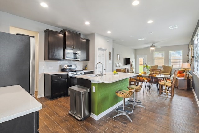 kitchen featuring wood finish floors, light countertops, appliances with stainless steel finishes, open floor plan, and a kitchen island with sink