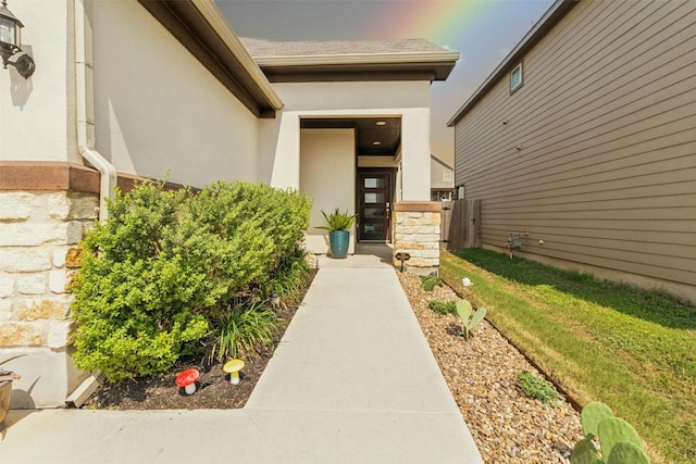 view of exterior entry featuring a yard, a shingled roof, and stucco siding