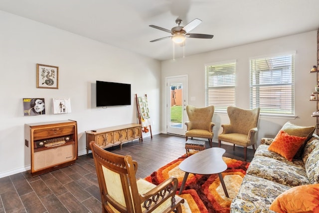 living area with dark wood-type flooring, a ceiling fan, and baseboards