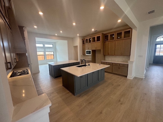 kitchen with hardwood / wood-style floors, built in microwave, sink, a kitchen island with sink, and black gas stovetop