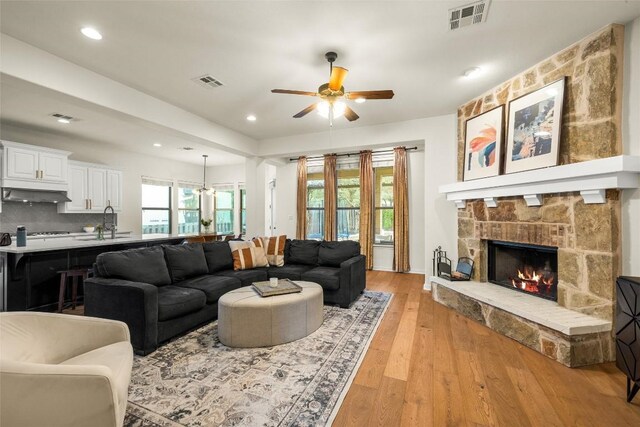 living room featuring a stone fireplace, sink, ceiling fan, and light hardwood / wood-style flooring