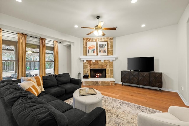 living room featuring hardwood / wood-style flooring, a stone fireplace, and ceiling fan