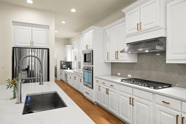 kitchen with sink, light wood-type flooring, stainless steel appliances, decorative backsplash, and white cabinets