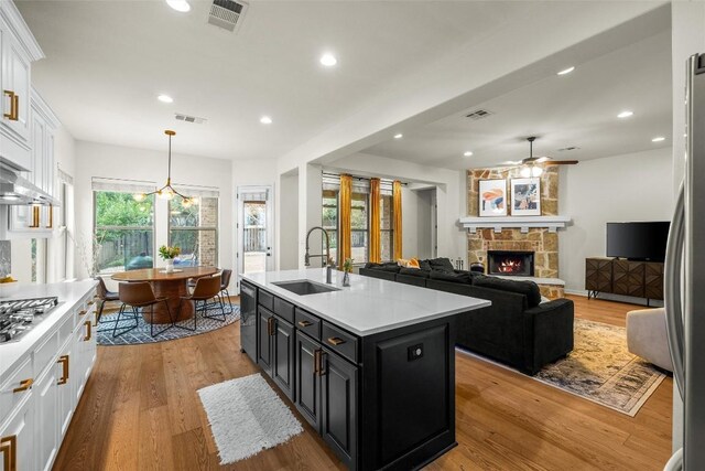 kitchen featuring sink, a kitchen island with sink, a fireplace, white cabinets, and light wood-type flooring