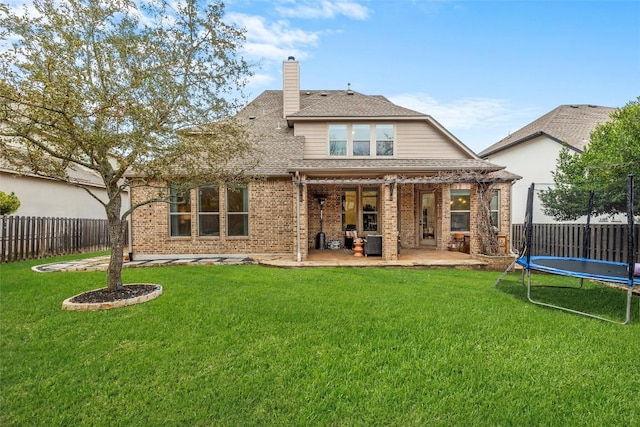 17408 Wildrye Dr, Austin, TX 78738 - rear view of property featuring a trampoline, a patio, a fenced backyard, brick siding, and a chimney